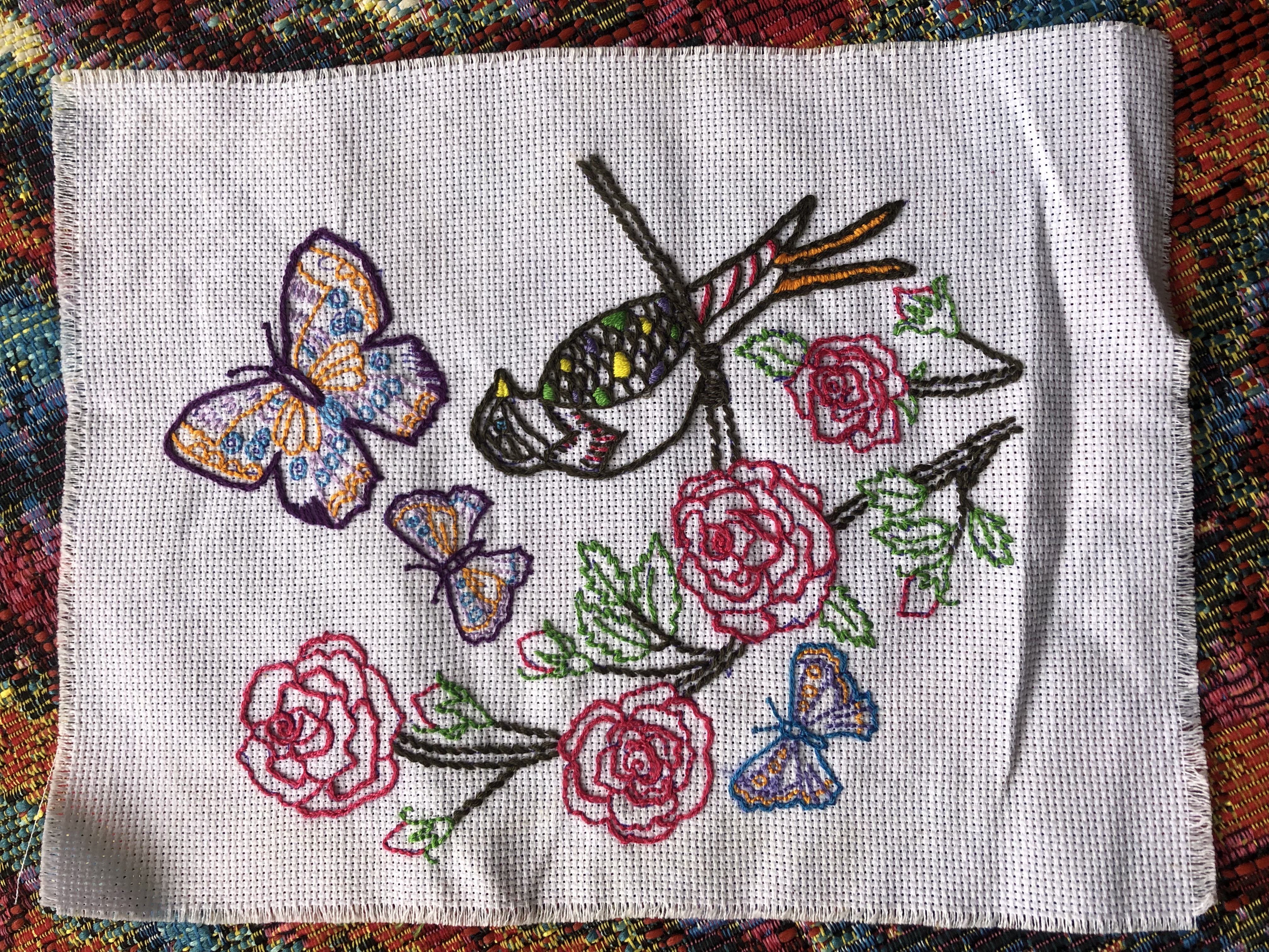 An embroidery. A
					bird is outlined sat on a tree branch