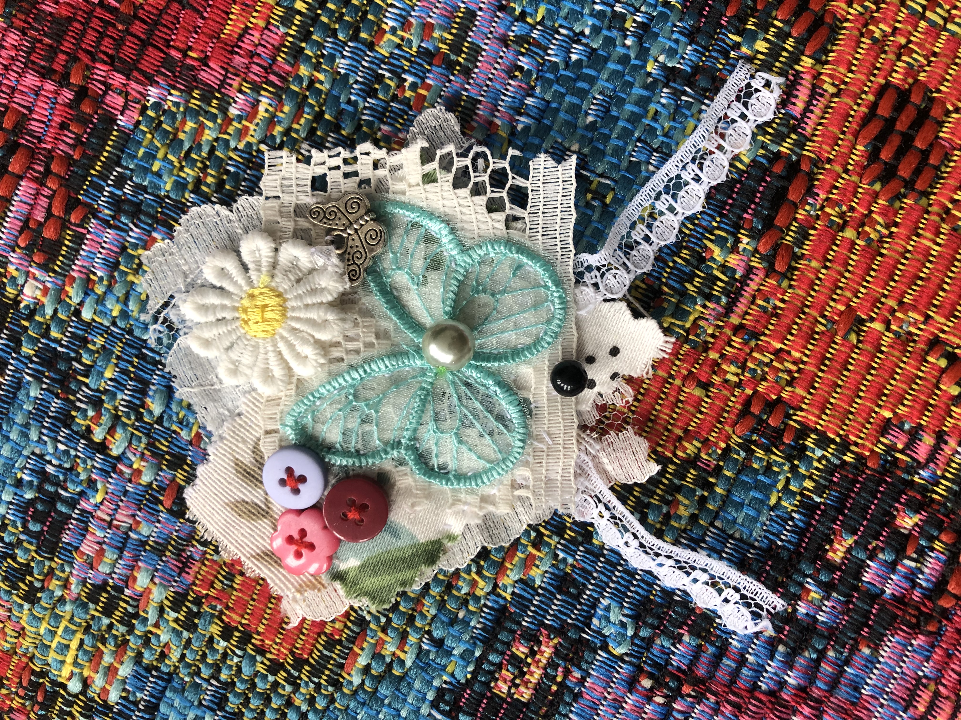 Scraps of fabric,
					mostly lace, have been fashioned into a heart shaped.
					Various buttons and a butterfly applique have been attached