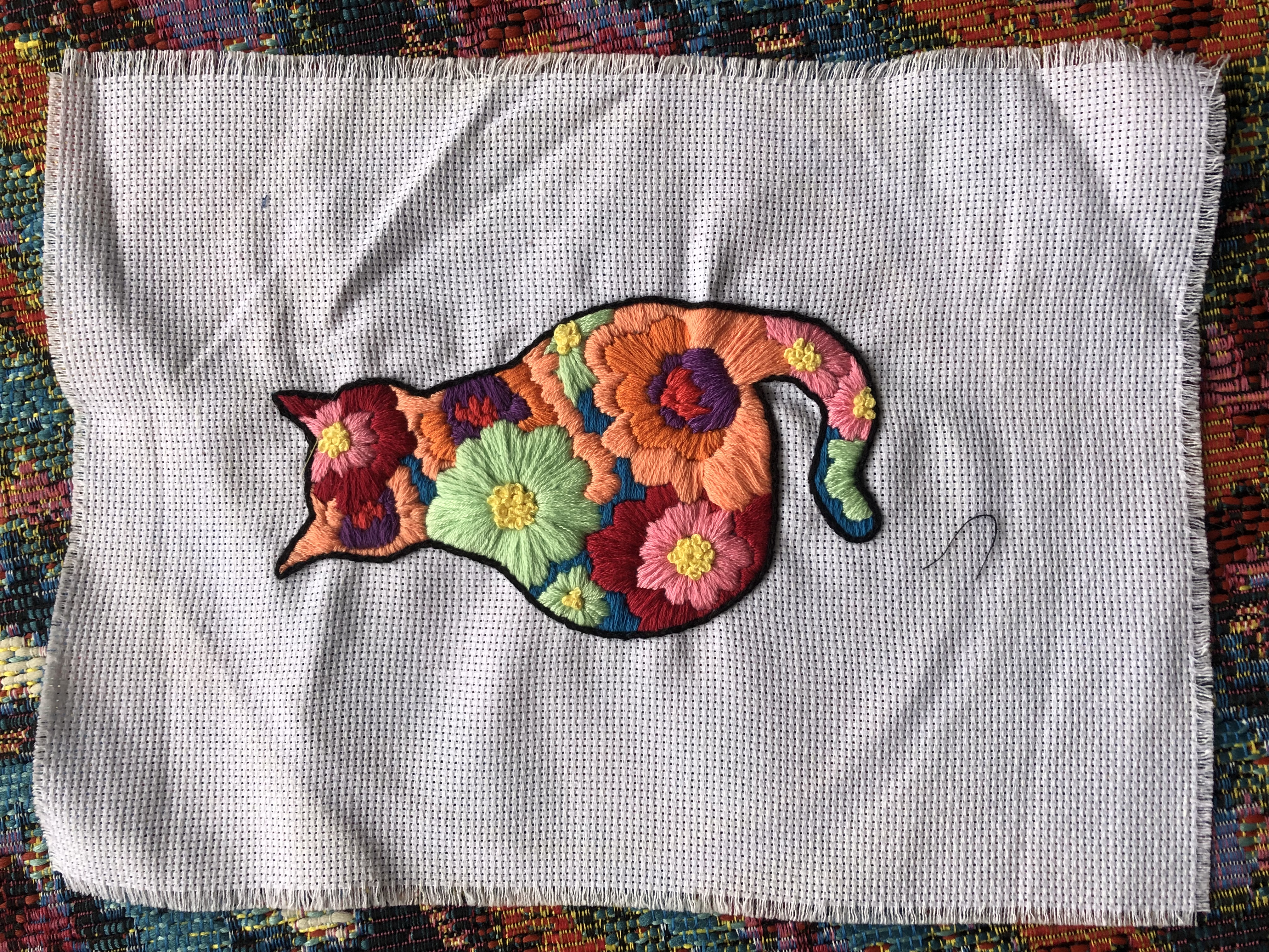 An embroidery. A cat is drawn filled
					in with flower shapes in different colours
